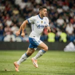Joueur de football professionnel en plein sprint sur un terrain de stade lors d'un match officiel